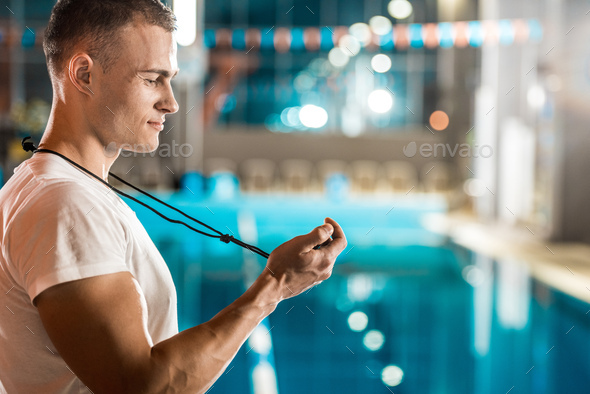 handsome swim trainer with stopwatch standing at competition swimming pool