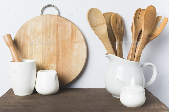 wooden kitchen utensils, ceramic cookware and cutting board on table