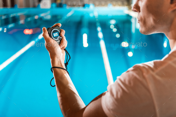 cropped view of swim trainer with stopwatch standing at competition swimming pool
