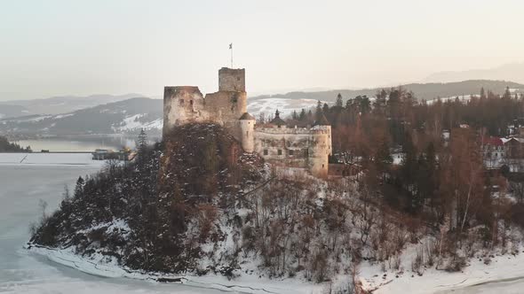 Idyllic Niedzica Castle at dusk on top of hill at frozen lake Czorsztyn, aerial alt