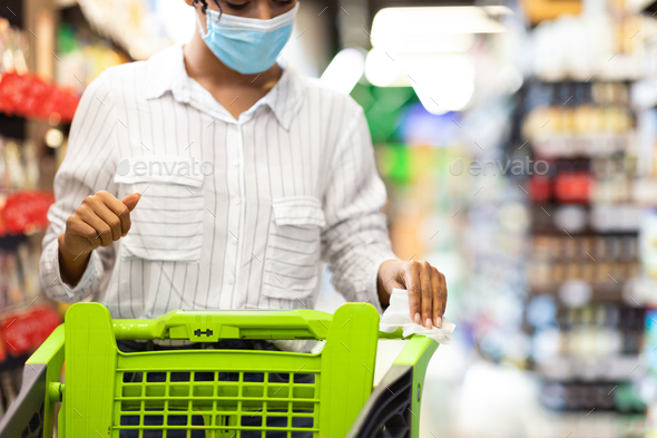 African Woman In Mask Disinfecting Shopping Cart In Grocery Store
