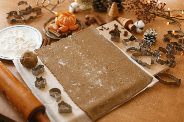 Making gingerbread cookies, christmas advent. Raw gingerbread dough, metal cutters ,flour, wooden rolling pin, spices, oranges, festive decorations on rustic table. Winter holidays tradition