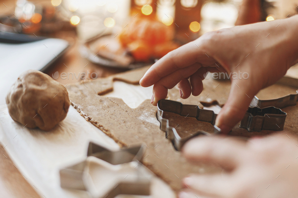 Hands cutting gingerbread dough with christmas tree metal cutter on rustic table with spices, festive decorations, lights. Person holding tree gingerbread cookie, Christmas holiday advent