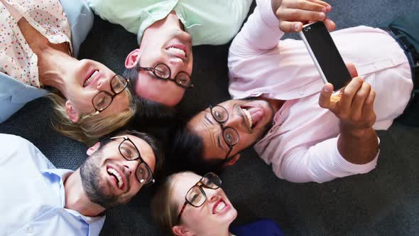 Business executive taking selfie from mobile phone while lying on the floor alt