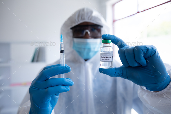 Health worker wearing protective clothes holding a vial bottle and syringe - Stock Photo - Images