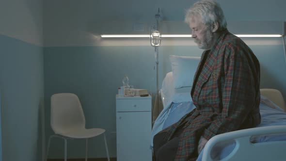 Sad lonely elderly man sitting on a hospital bed at night