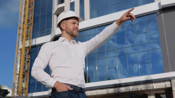 Engineer Architect in a White Shirt and Helmet on the Background of a Modern Glass Building Manages alt