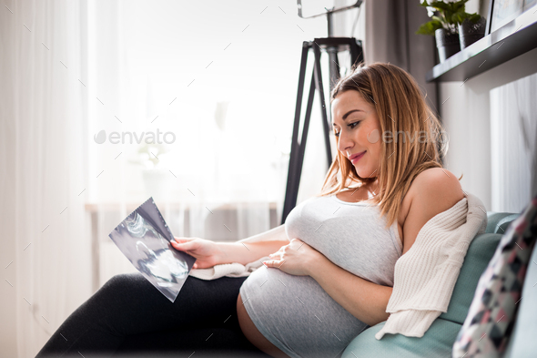 Pregnant woman on sofa looking her baby on ultrasound image, usg photo - Stock Photo - Images