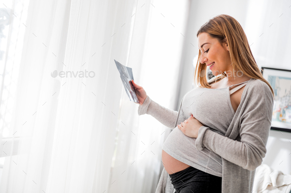 Pregnant woman at home looking her baby on ultrasound image, usg photo - Stock Photo - Images