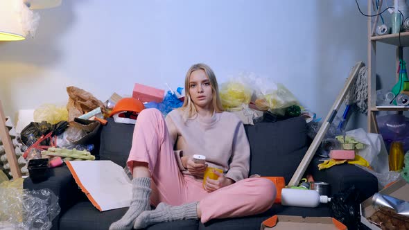 Woman sitting on the sofa with trash and garbage around her