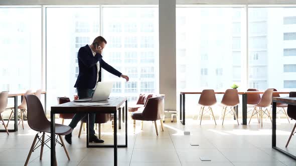 Concentrated Young Businessman Is Walking Around the Office and Talks on Phone alt