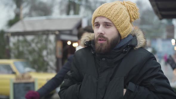 Handsome Caucasian Man in Yellow Hat Standing on Winter Street As His Beautiful Girlfriend or Wife alt