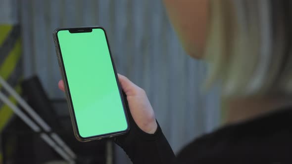 Over shoulder shot of caucasian girl with blond hair sitting on sofa and holding smartphone alt