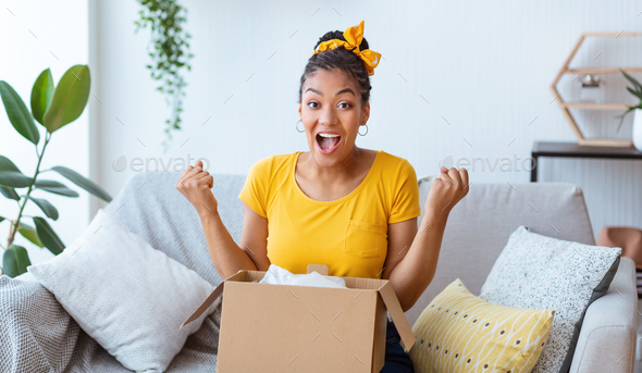 Excited black lady unpacking parcel after online shopping