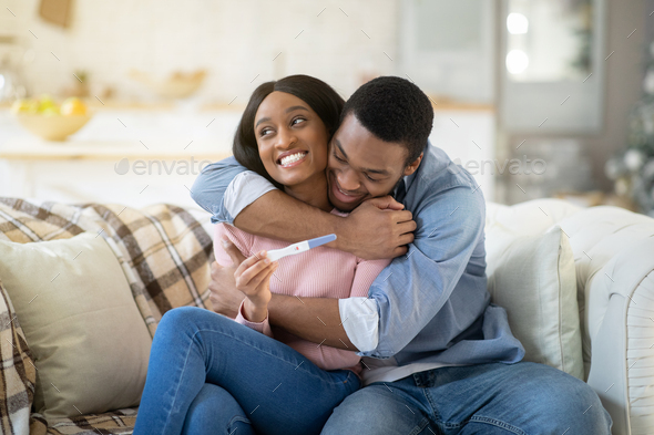 Loving black husband hugging his wife with positive pregnancy test at home