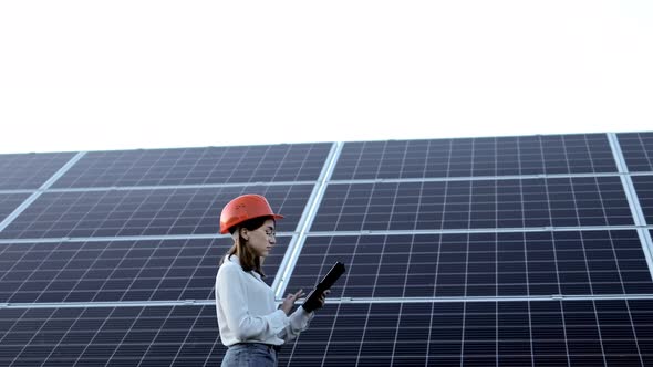 Beautiful young engineer standing near solar panels outdoors, Green Energy Concept alt