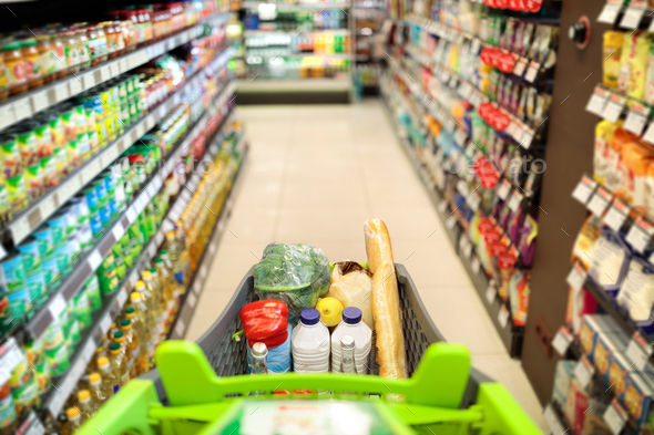 Shopping Cart Full Of Food Products Over Supermarket Aisle Background