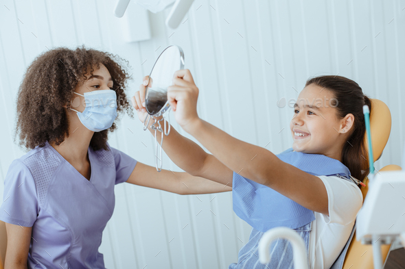 Happy small girl looks in mirror for estimating dentist work and enjoying result - Stock Photo - Images