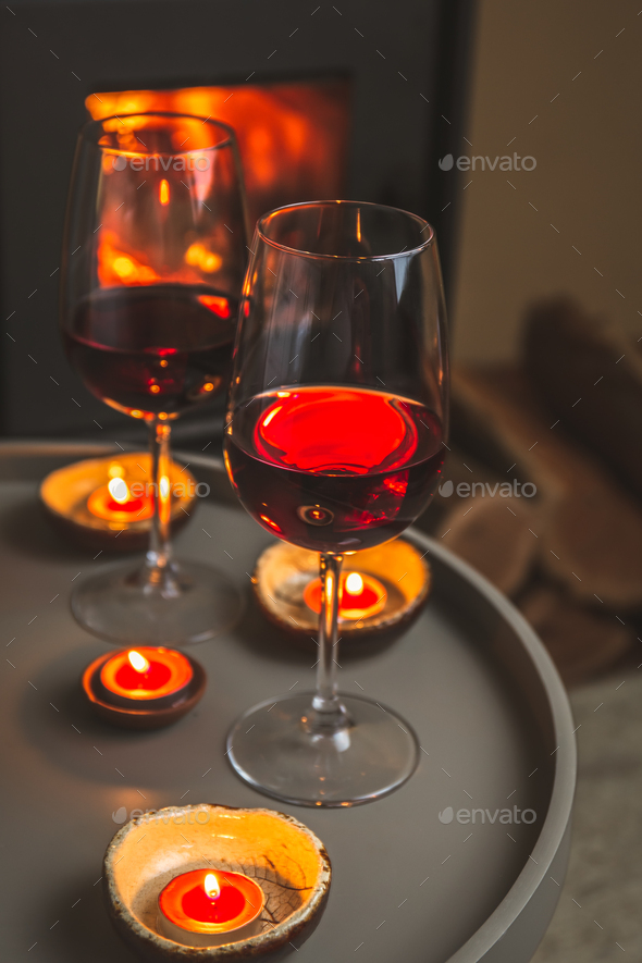 Two glasses of red wine front of fireplace. Romantic light.