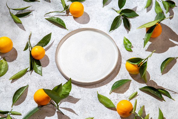 Whole oranges witl orange tree leaves on white background around empty plate. top view, flat lay - Stock Photo - Images