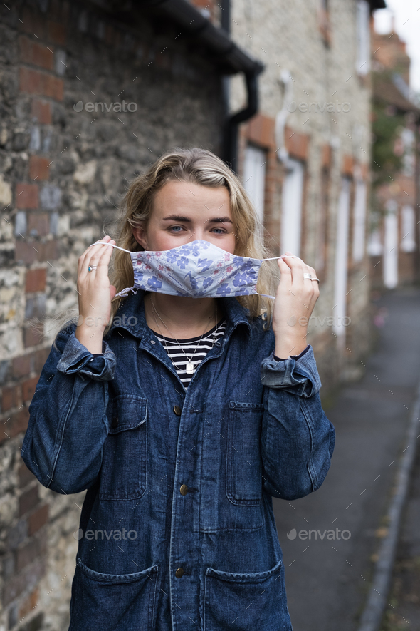 Young blond woman standing outdoors, putting on face mask.