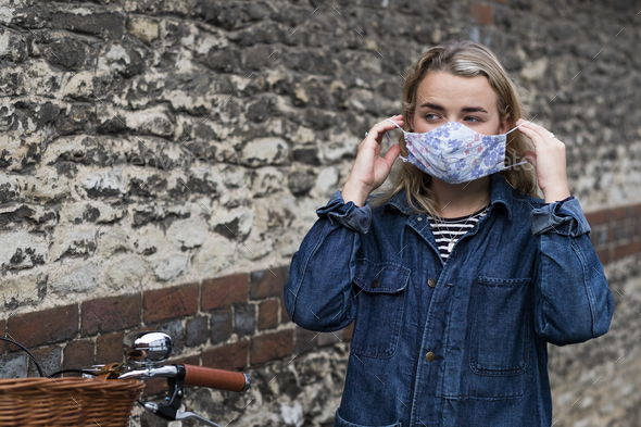 Young blond woman standing outdoors, putting on face mask.