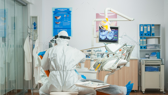 Dentist and assistant in coverall examining mouth of patient