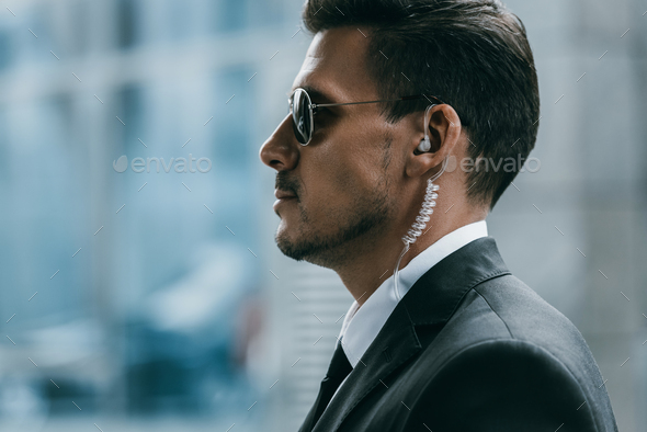 profile of handsome security guard with sunglasses and security earpiece - Stock Photo - Images