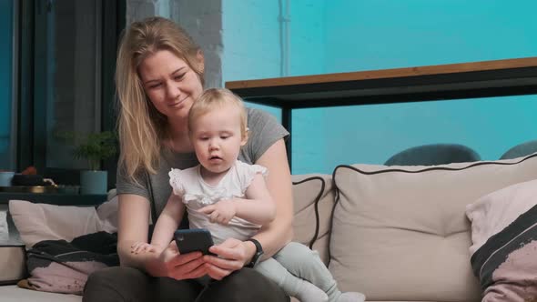 Young Mother in a Gray T-shirt Orders Food on Phone, Her Daughter Also Looks at Phone and They Happy alt