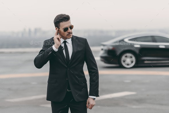 serious bodyguard listening message with security earpiece on helipad - Stock Photo - Images