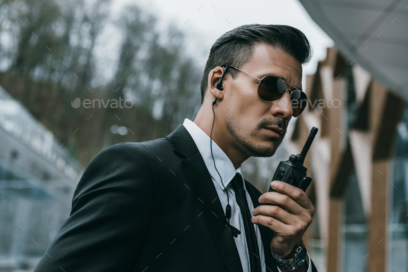 serious handsome security guard talking by portable radio - Stock Photo - Images