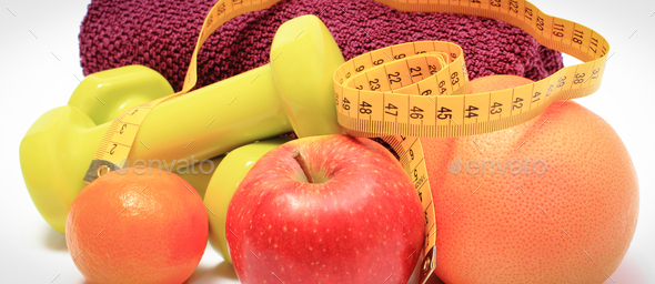 Tape measure, fresh ripe fruits and dumbbells using in fitness. Slimming, healthy nutrition and sporty lifestyles