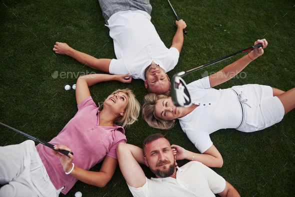 Four people, two guys and two girls, lie on the golf course and relax after the game