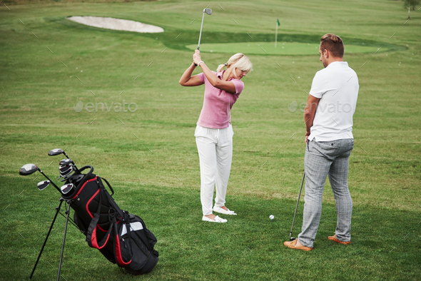Girl playing golf and hitting by putter on green