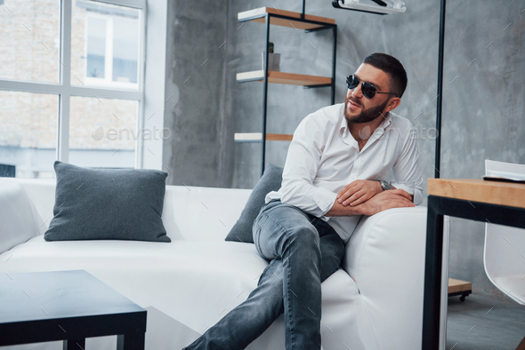 Young short-haired man in sunglasses sitting on couch in the office