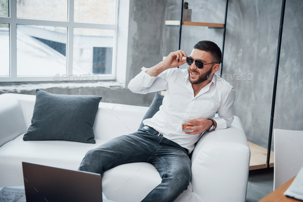 Young short-haired man in sunglasses sitting on couch in the office