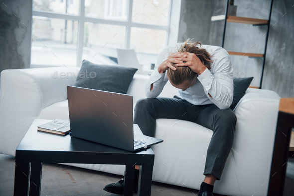 Stressed man sitting at couch in front of laptop have lowered his head