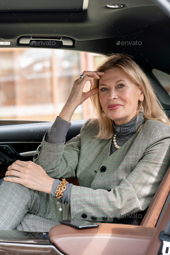 Smiling elegant businesswoman looking at you from backseat of taxi cab