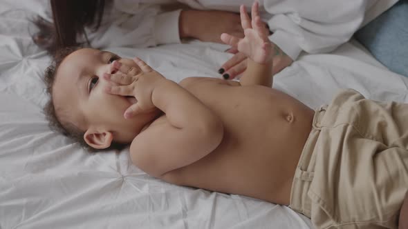 Cute Mixedrace Baby Laying Down on Bed and Playing with His Parents alt