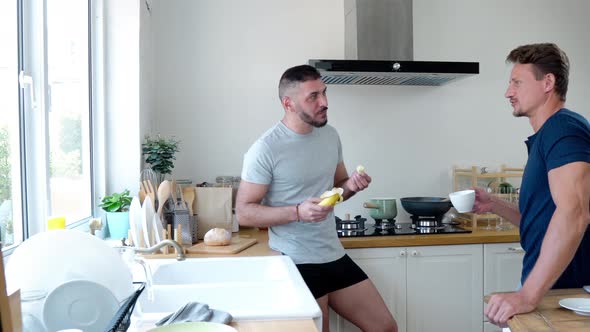 Young fit happy handsome gay male couple talking and laughing in kitchen