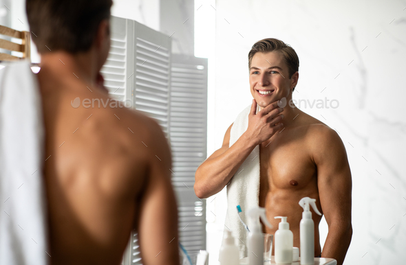 Confident young man looking in the mirror, touching chin