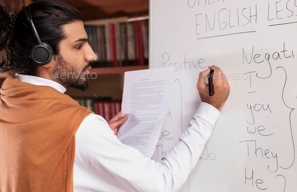 Arab Teacher Teaching English Writing Grammar Rules On Blackboard Indoors