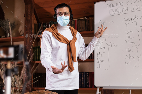 Teacher In Mask Making Video Lecture Pointing At Blackboard Indoor