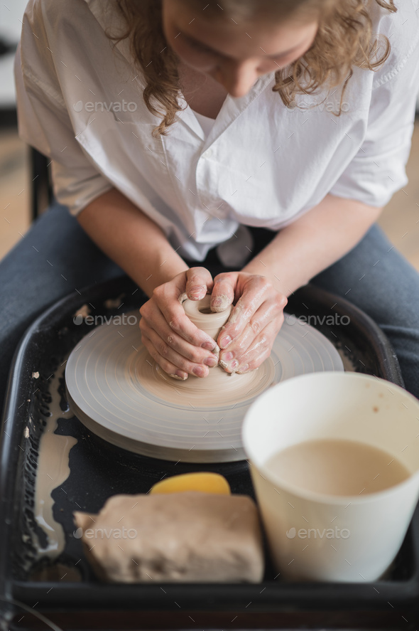 Woman working on potters wheel making dishes with their own hands. Close-up photo of dirty hands