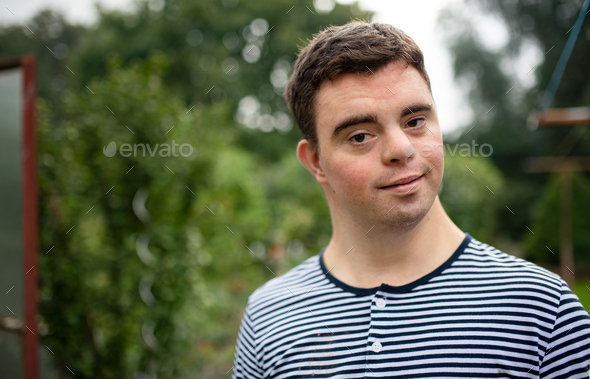 Portrait of down syndrome adult man standing outdoors in garden. Stock