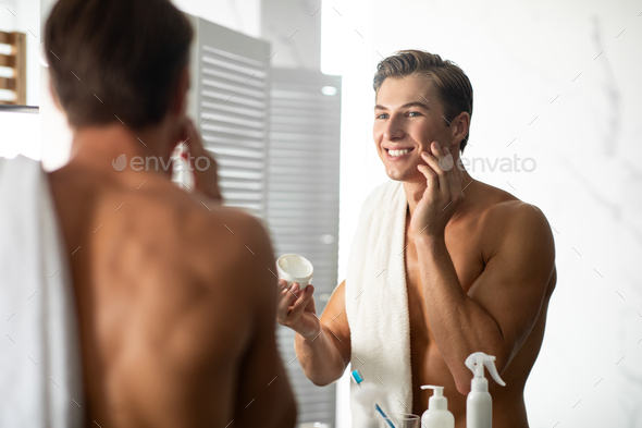 Handsome guy looking in the mirror applying cream