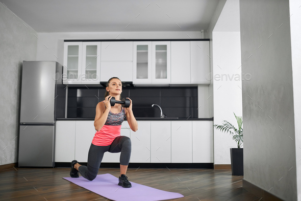 Fit young woman practicing lunges at home using dumbbell