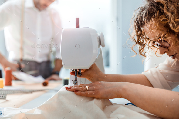 Professional dressmaker woman sews clothes on sewing machine at fashion  design workshop Stock Photo by leszekglasner