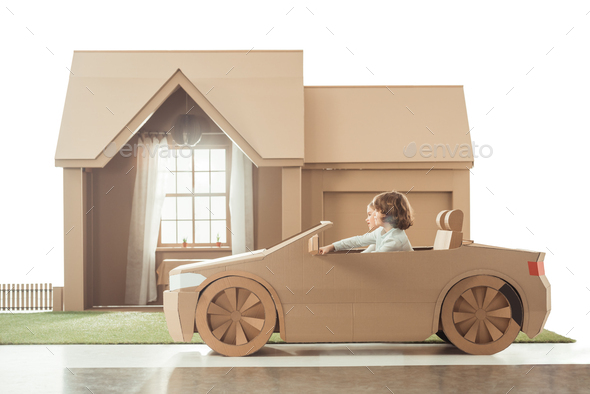 side view of kids riding cardboard car in front of house isolated on white