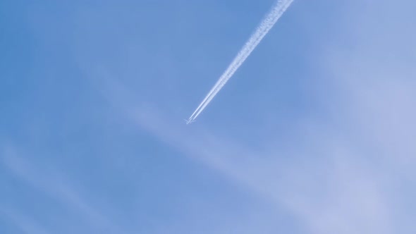 Distant Passenger Jet Plane Flying on High Altitude on Blue Sky with White Clouds Leaving Smoke alt